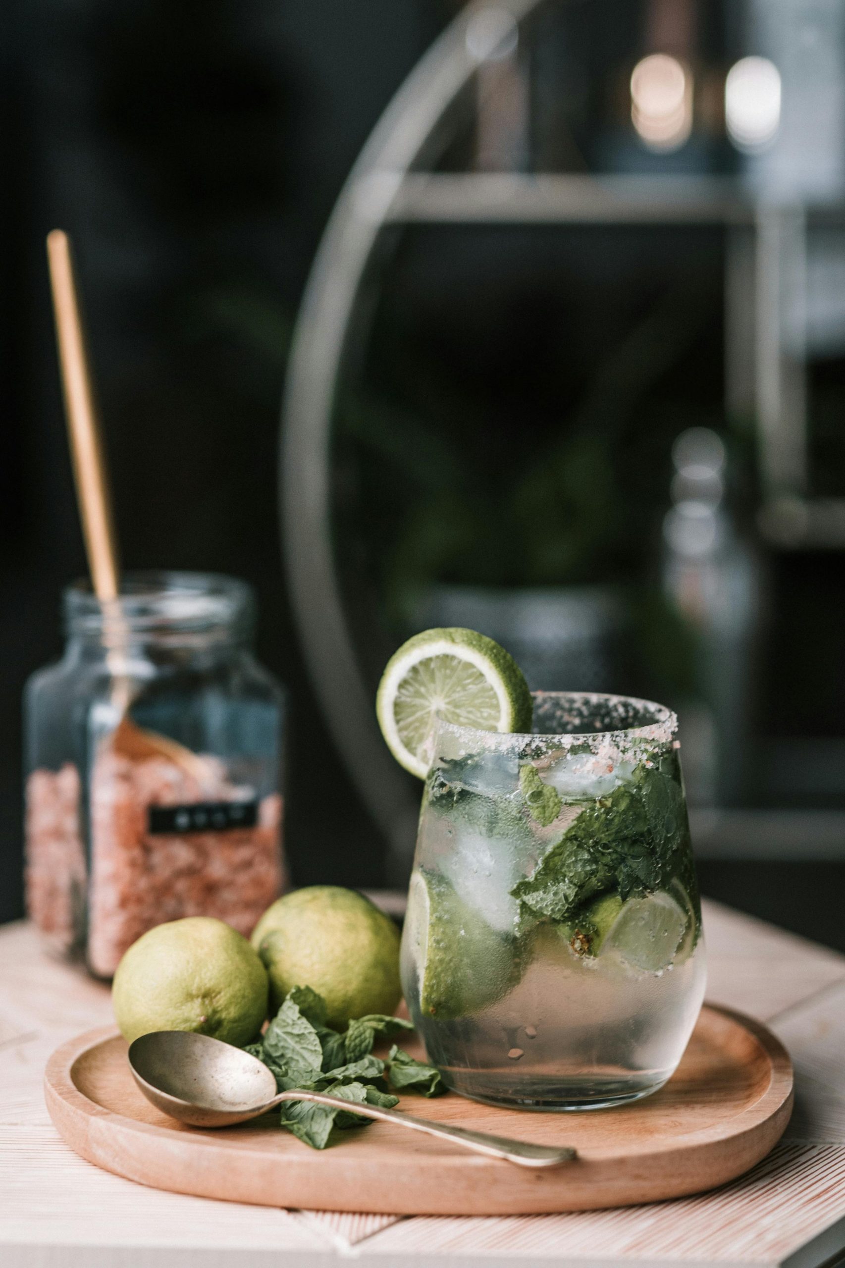 A close-up of a refreshing mojito cocktail with lime and mint leaves on a wooden tray, perfect for a cool summer drink.